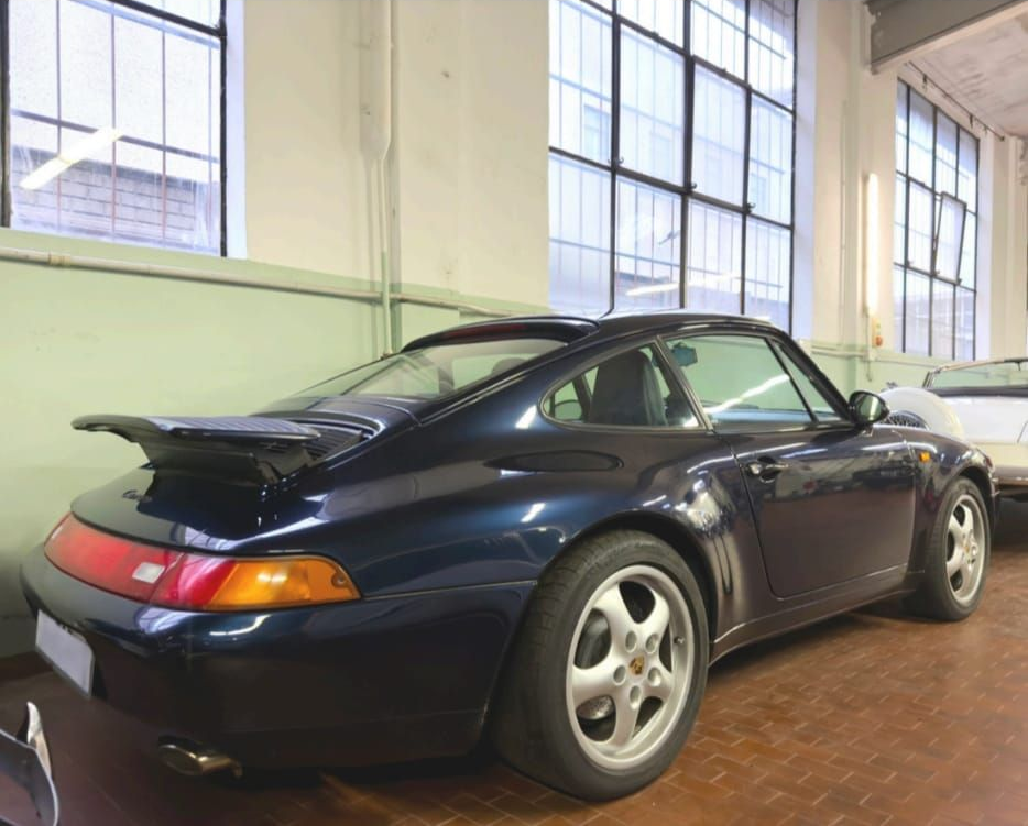 Porsche 911 blu scuro in uno showroom interno luminoso, vista posteriore a tre quarti