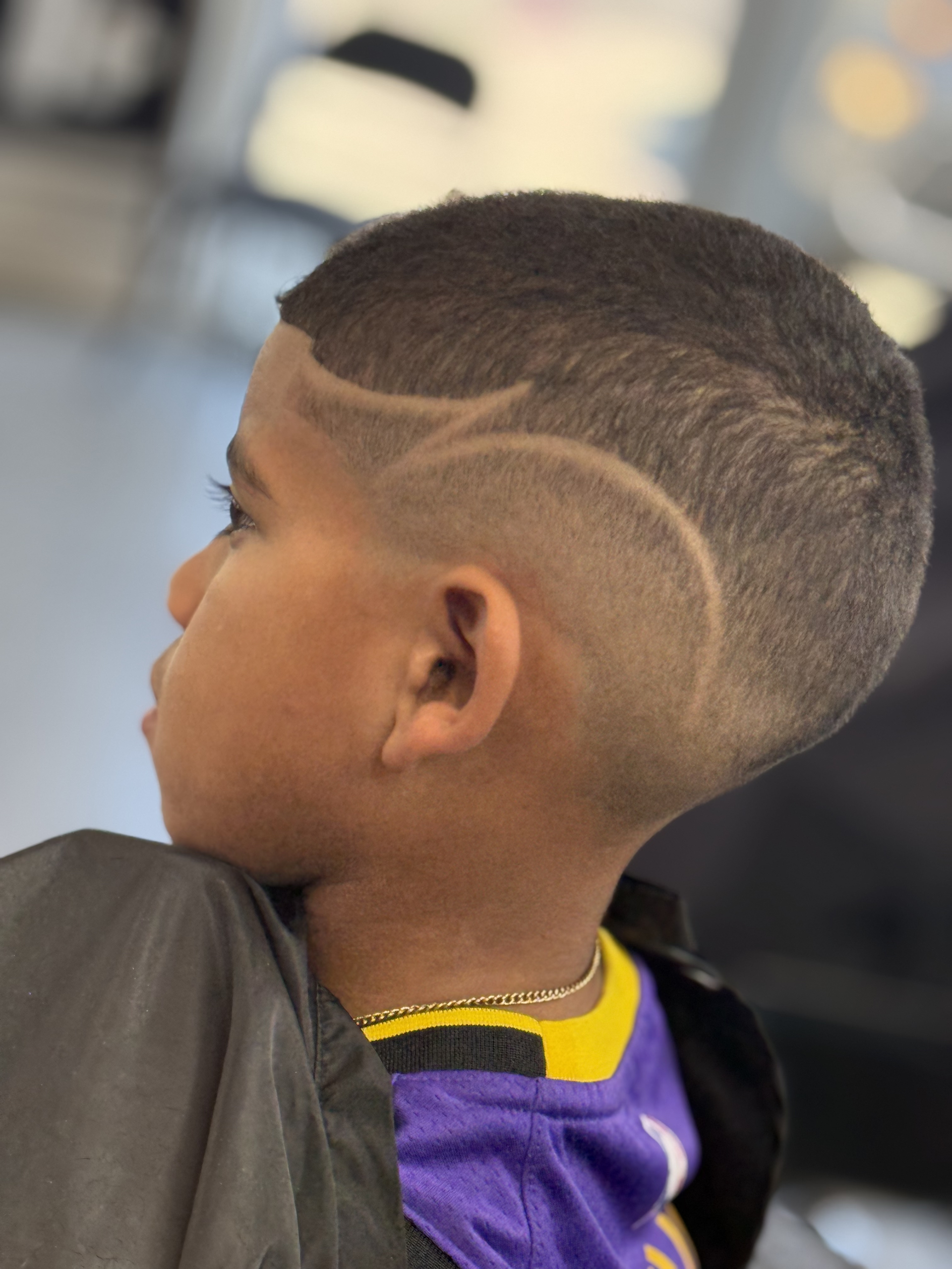A profile view of a person with a short, faded haircut featuring a shaved curved line design on the side of the head.