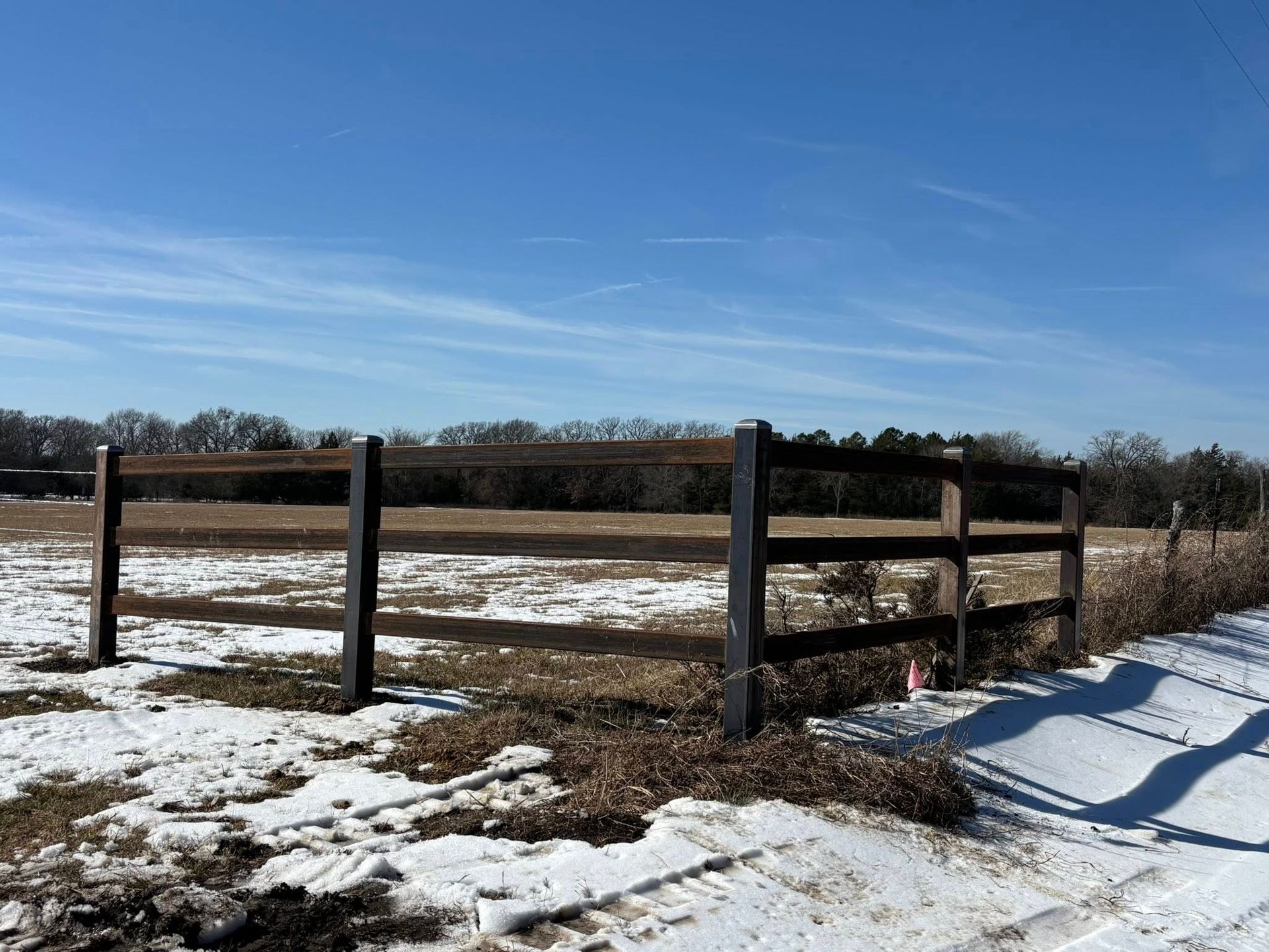 Snowy rural field with a wooden fence under a clear blue sky