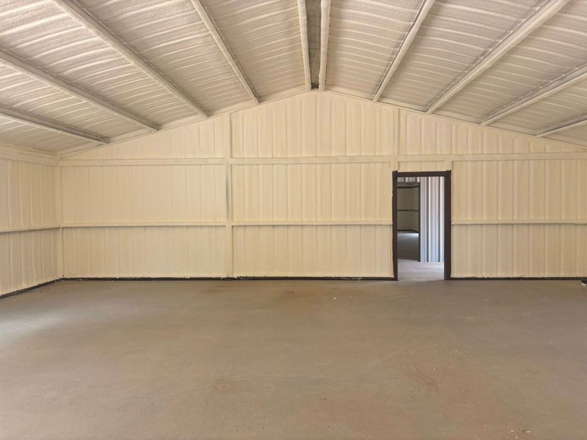 Empty beige metal shed interior with a concrete floor and a doorway on the back wall