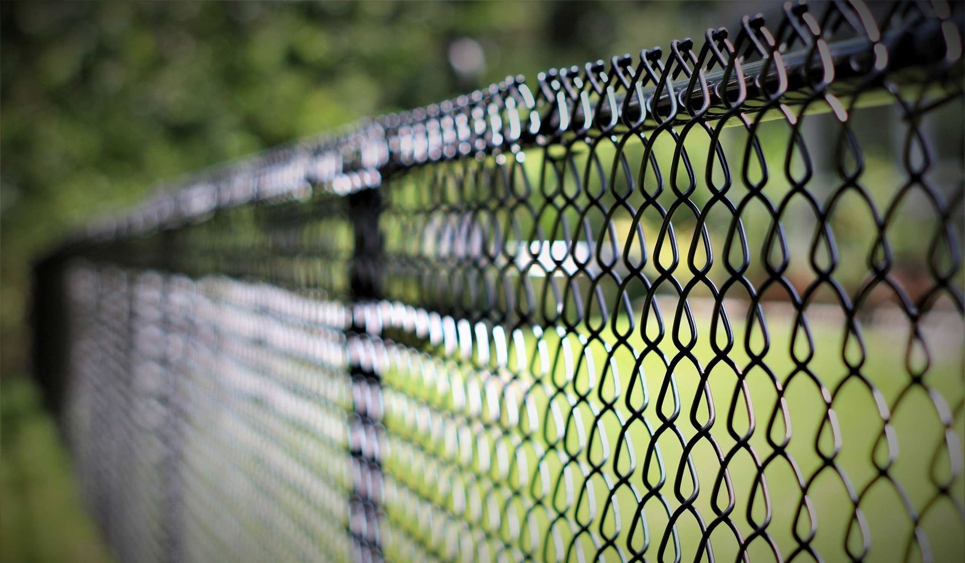 Close-up of a black chain-link fence with a blurred green field in the background