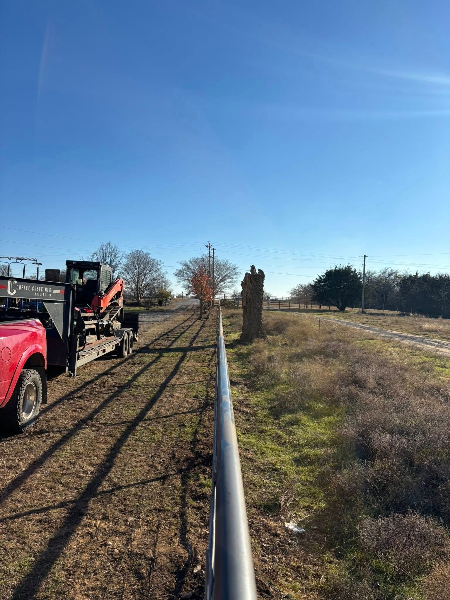 Fenced grassy field with a red truck and trailer on the left under a clear blue sky