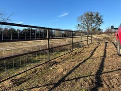 A fenced dirt path beside a field under a clear blue sky, with a red vehicle at right.