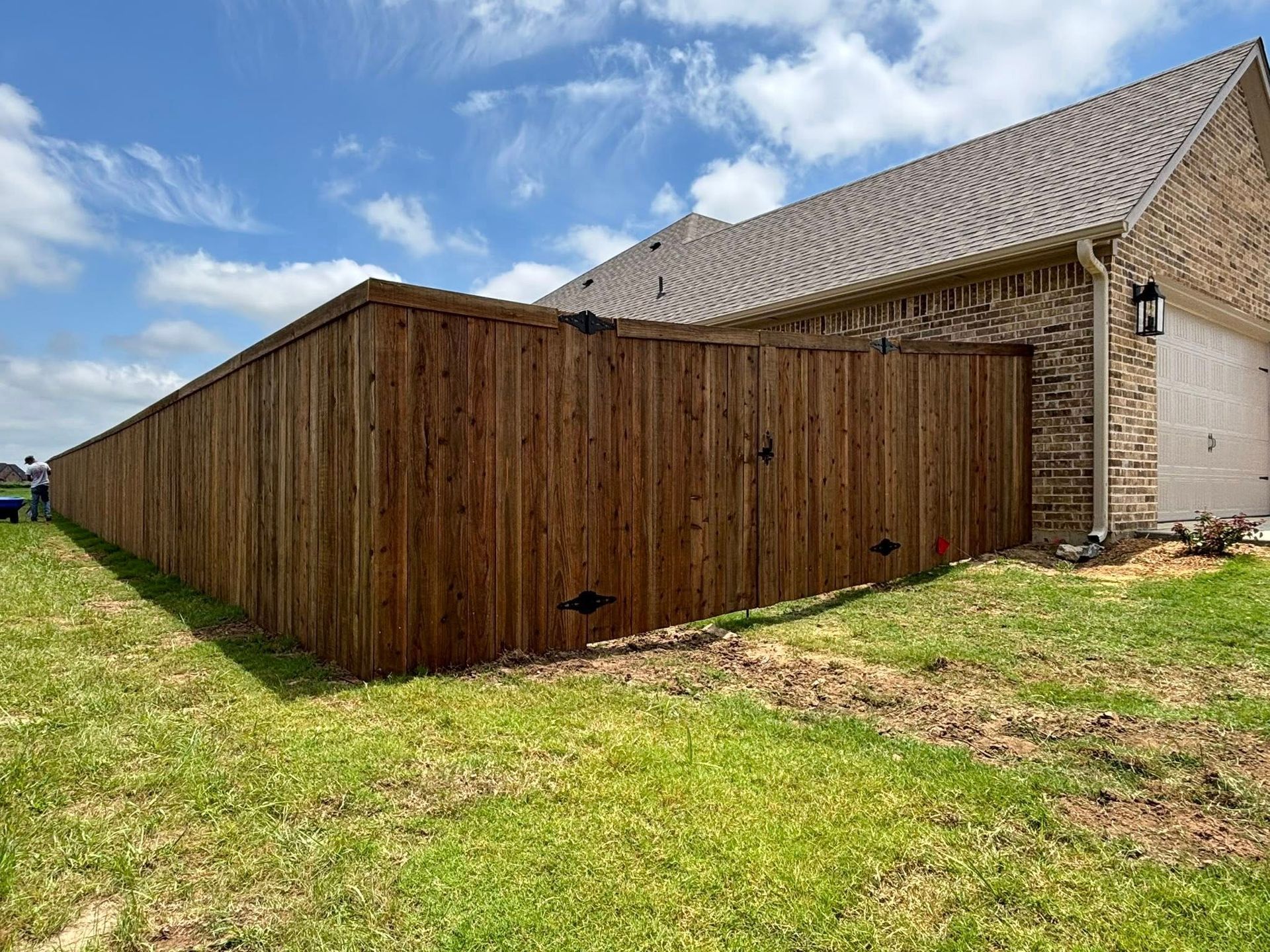 Wooden fence enclosure beside a stone house on a grassy yard under a cloudy sky