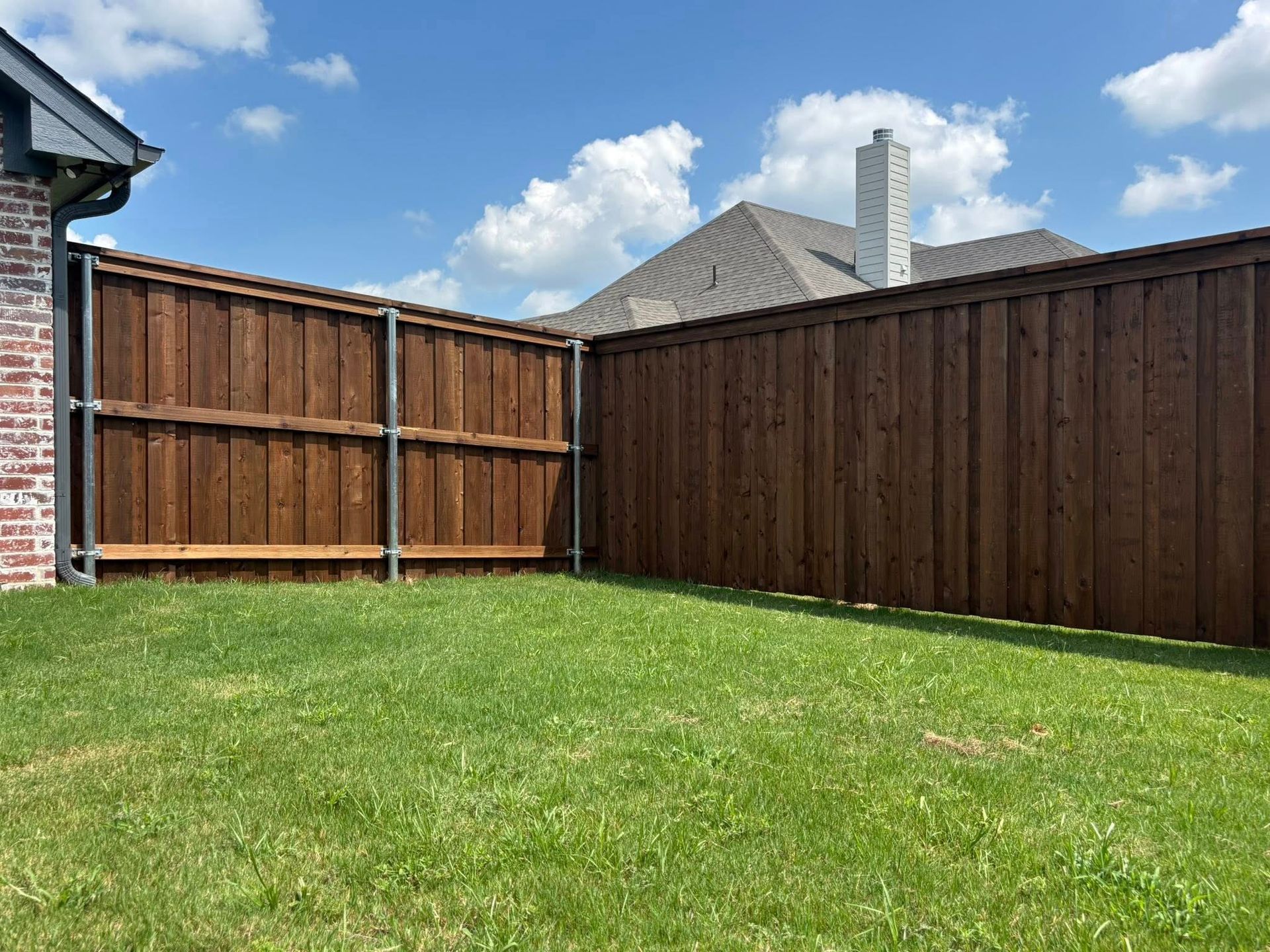 Backyard with green lawn, wooden privacy fences, and a blue sky with clouds