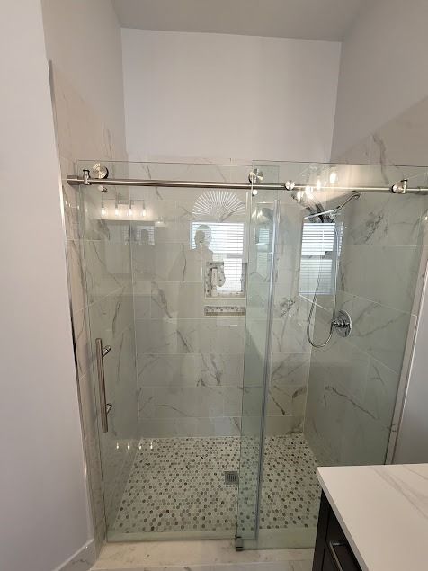 A modern bathroom with a glass shower, marble-like tiles, and a pebble-stone floor