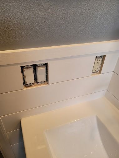 Light switches and outlet installed in white shiplap above a bathroom sink