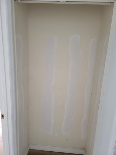 Empty closet with spackling on off-white walls, door frame on the left and right