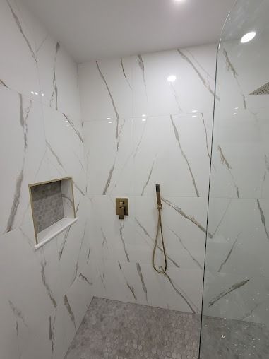 White marble tile shower with a golden showerhead and glass door