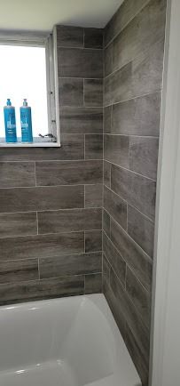 Bathroom with wood-look tile walls, white bathtub, and window with blue bottles
