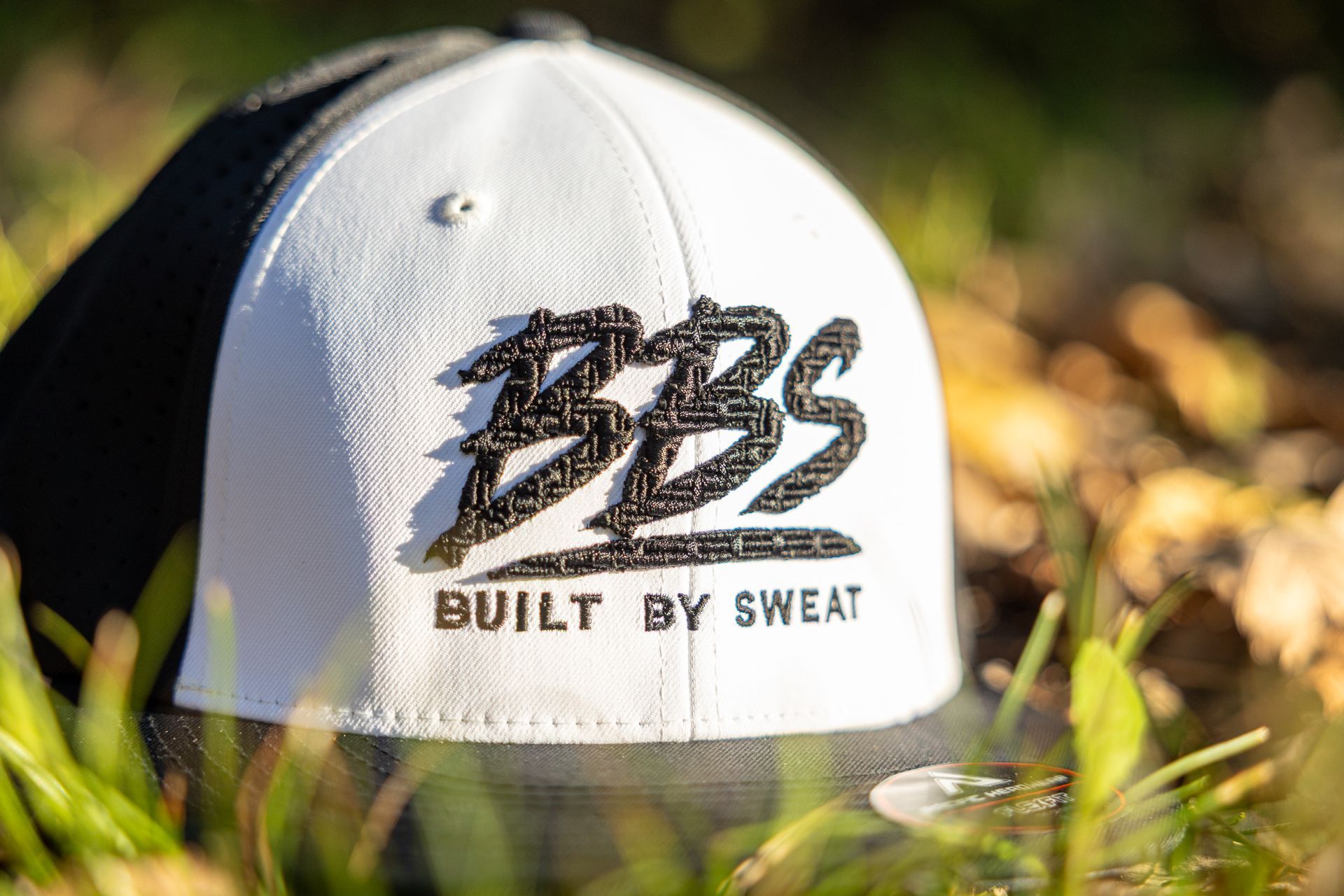 Black cap embroidered with orange “BBS” logo, resting in grass outdoors