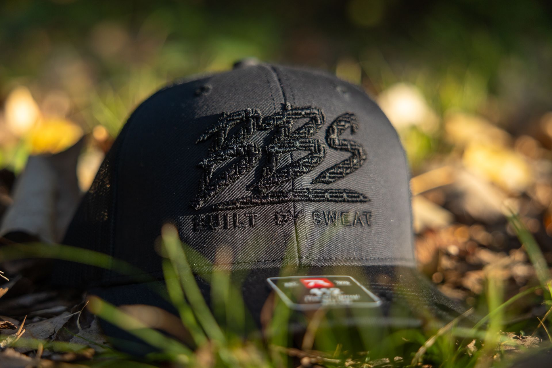 Tan mesh cap with black “BBS” logo and “BUILT BY SWEAT” text in sunlight among grass