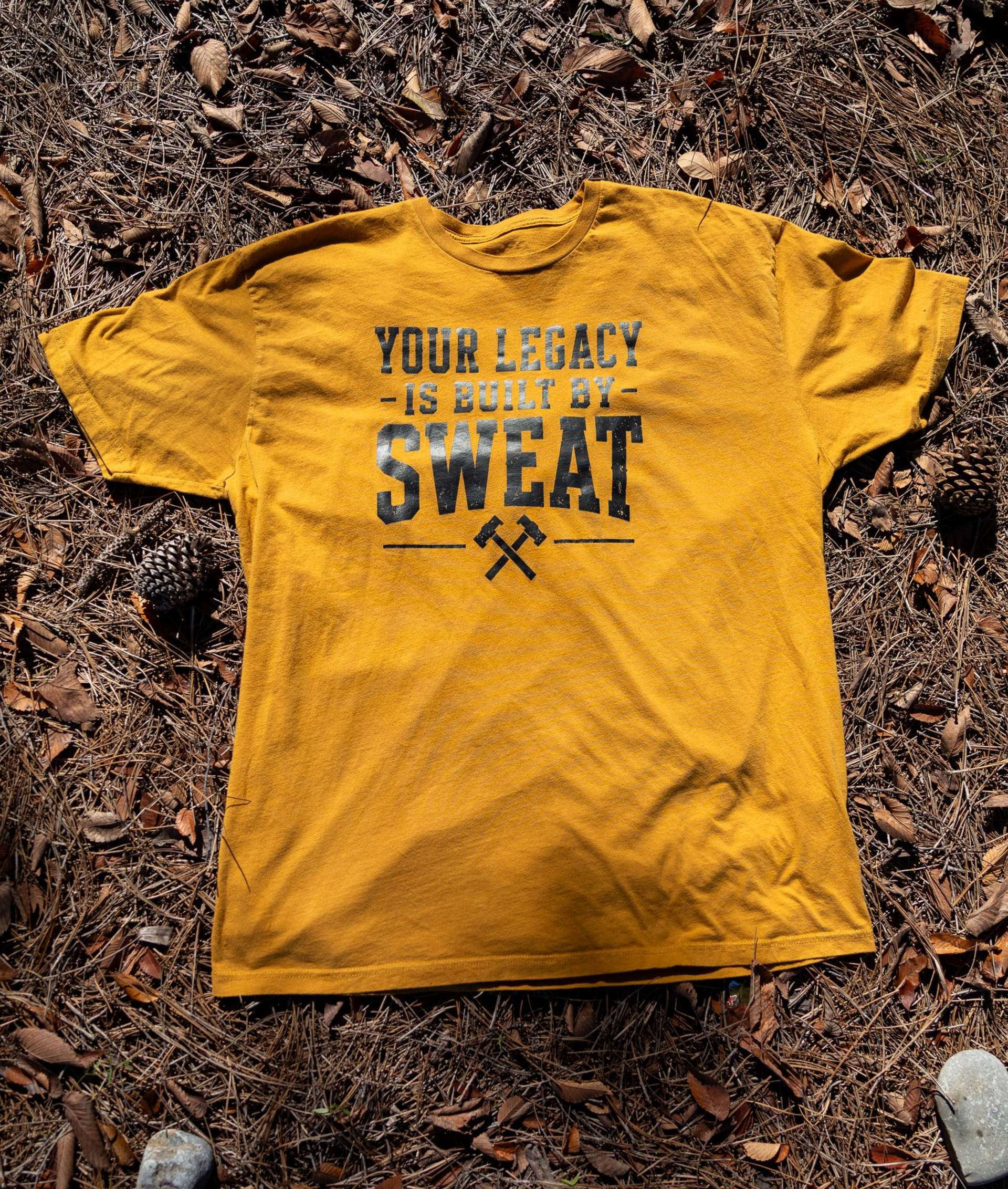 Yellow T-shirt on brown leaves with text: “Your legacy is built by sweat.”