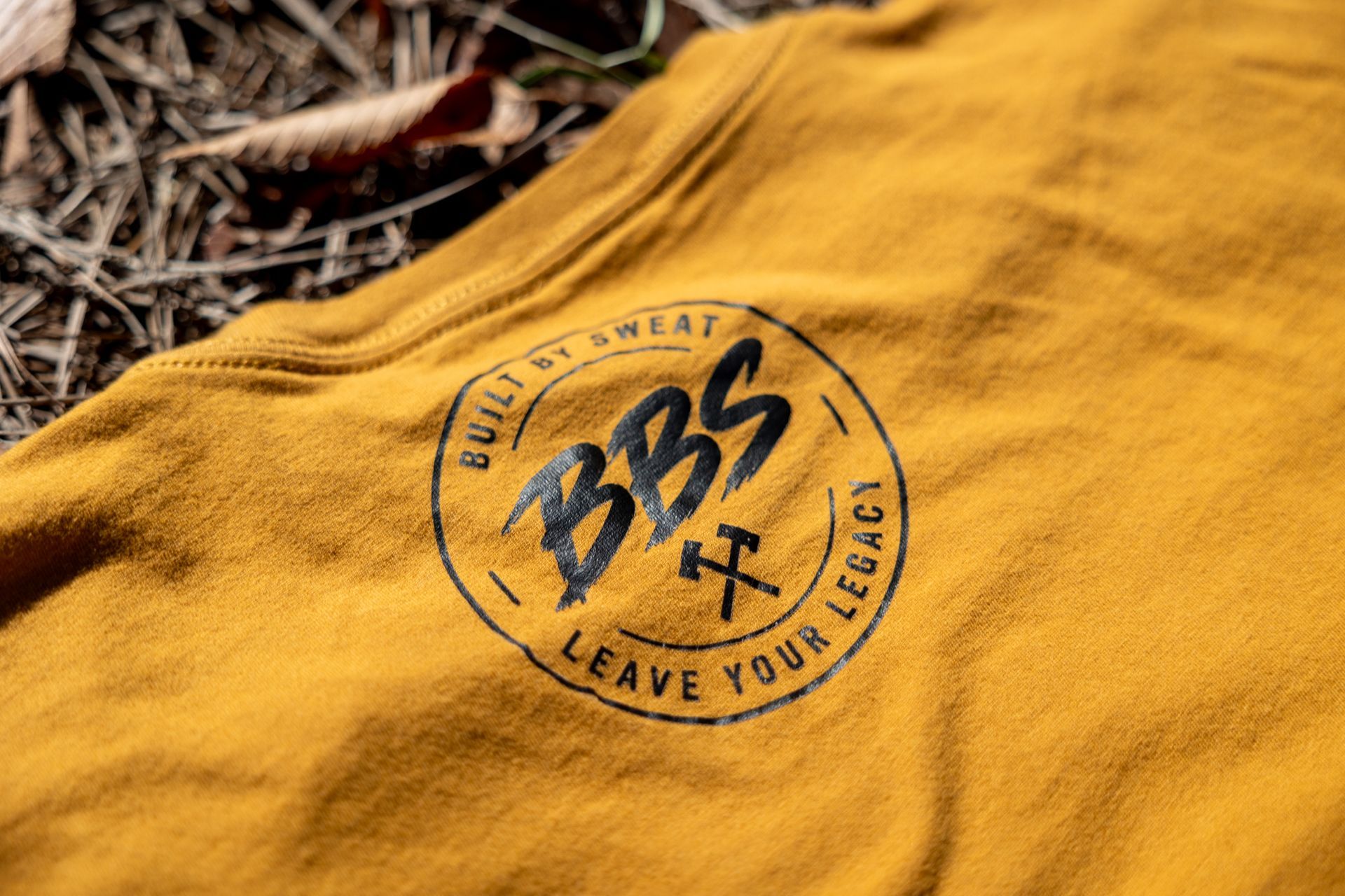 Yellow T-shirt on brown leaves with text: “Your legacy is built by sweat.”