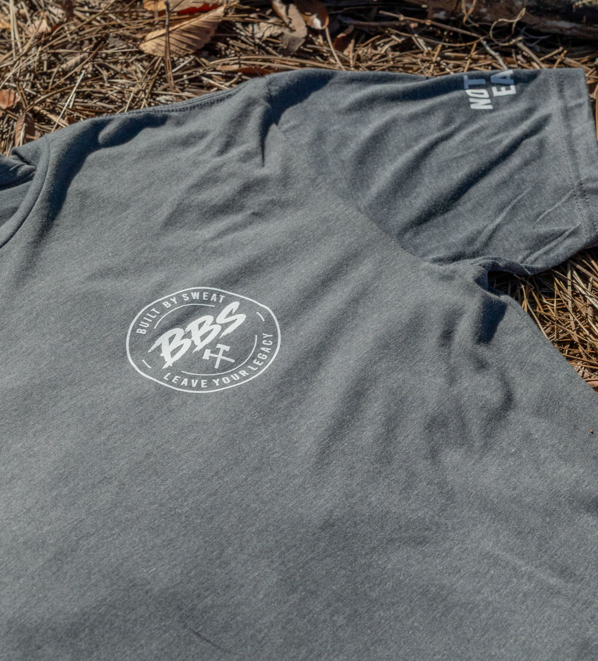 Gray T-shirt with white text lying on brown leaves outdoors