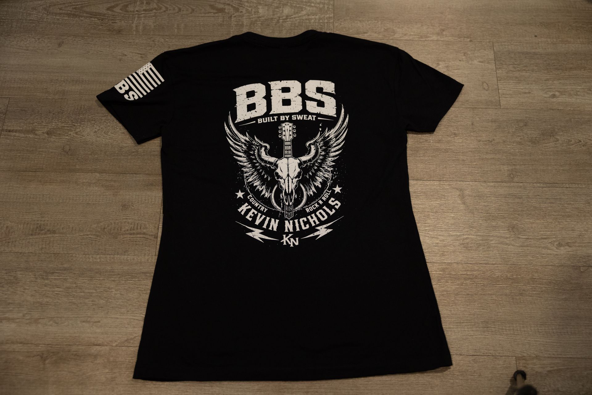 Black graphic T-shirt with white BBS eagle design laid flat on a wooden floor.