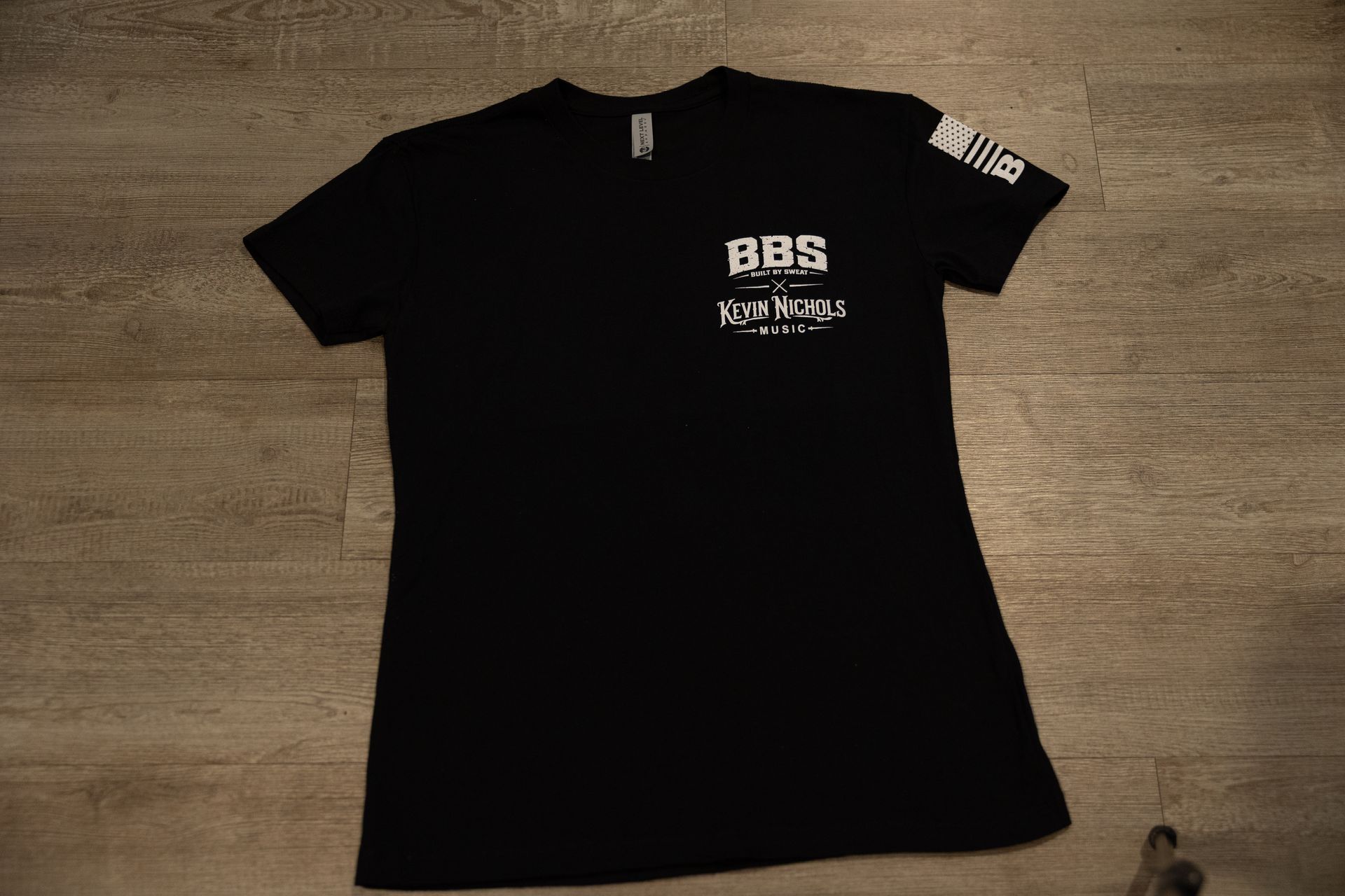 Black graphic T-shirt with white BBS eagle design laid flat on a wooden floor.