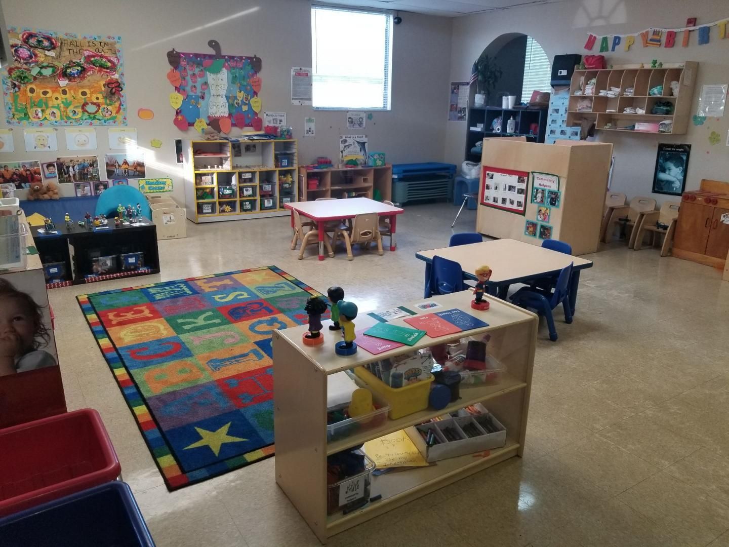A classroom with tables and chairs and a colorful rug