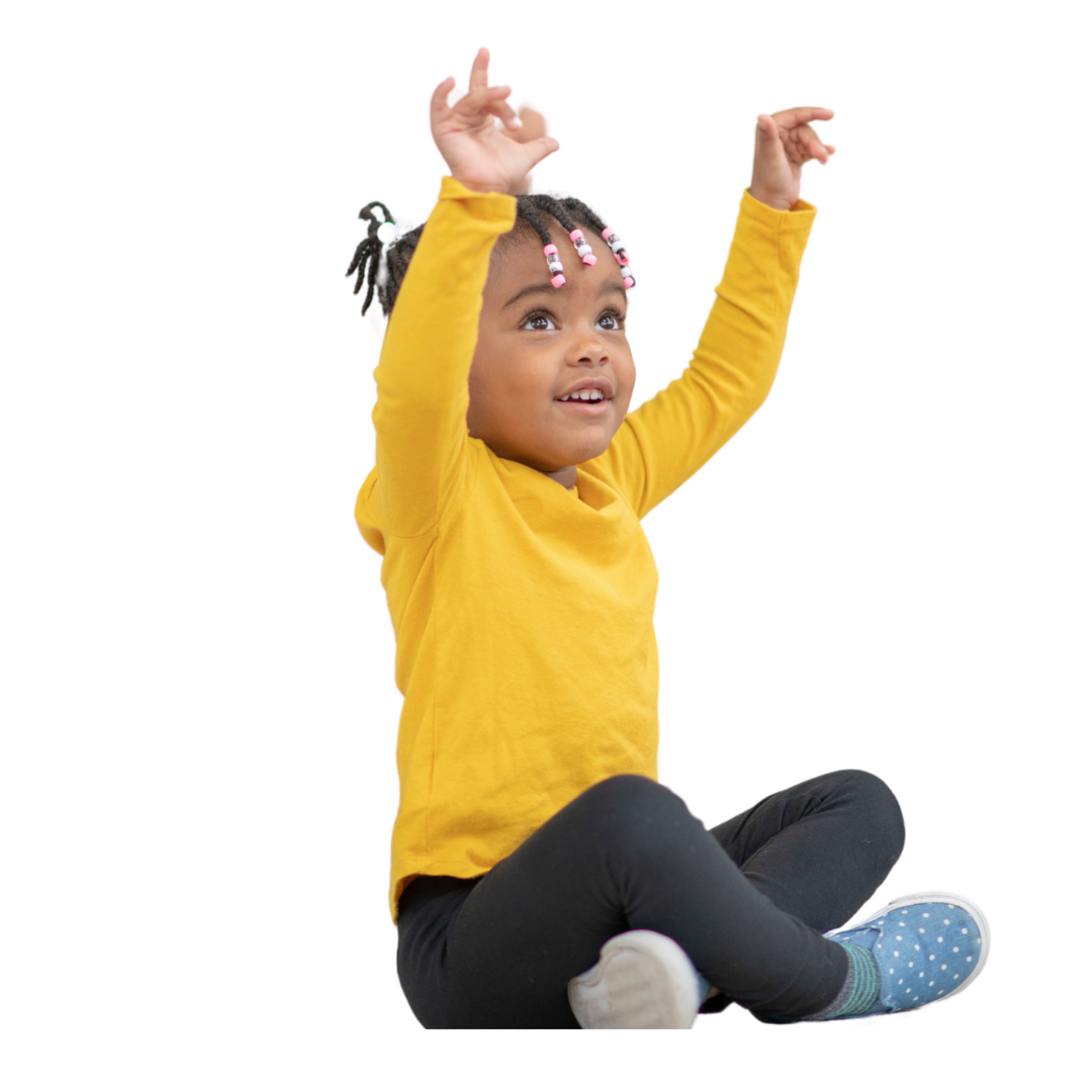 A little girl in a yellow shirt is sitting on the floor with her arms in the air