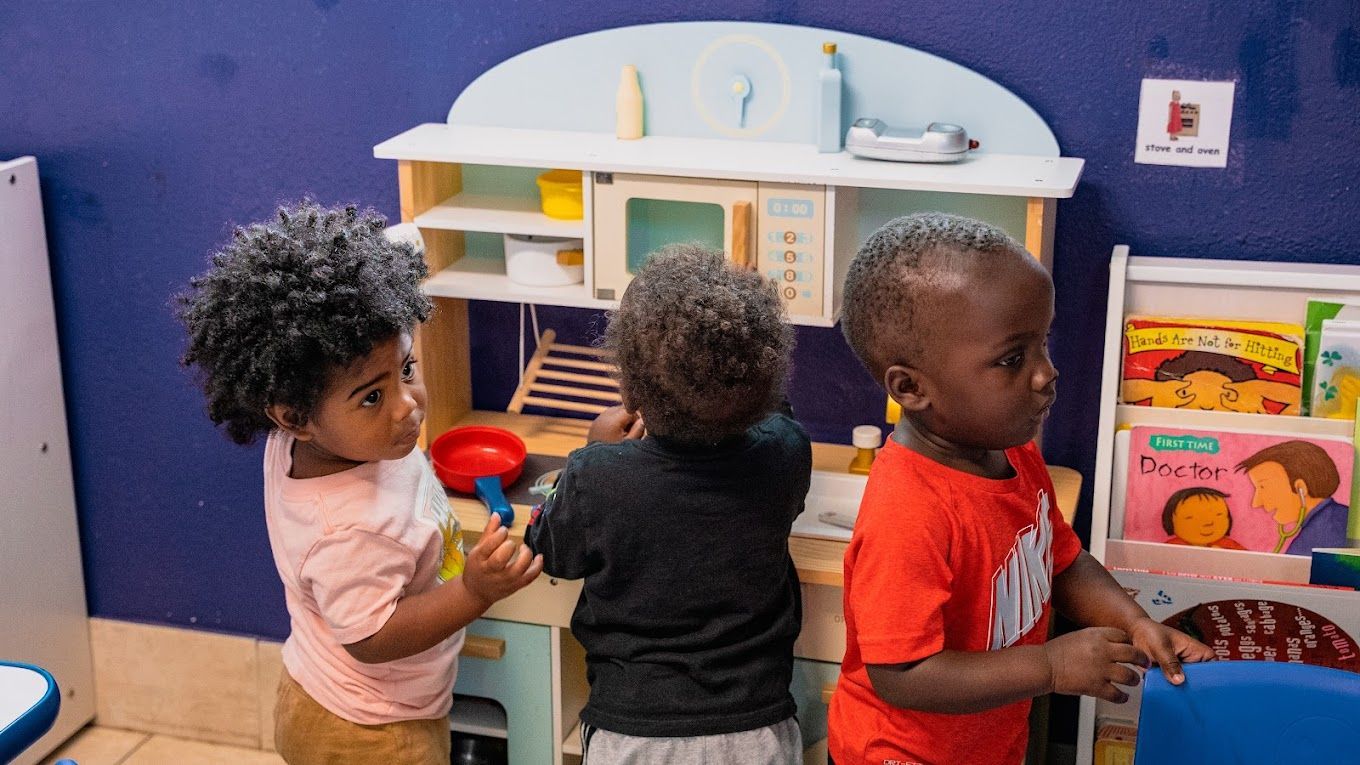Three young children are playing in a room with a toy kitchen.
