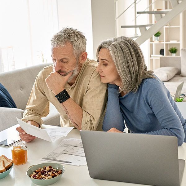 A man and woman looking at paperwork and a computer at a dining table in their home.