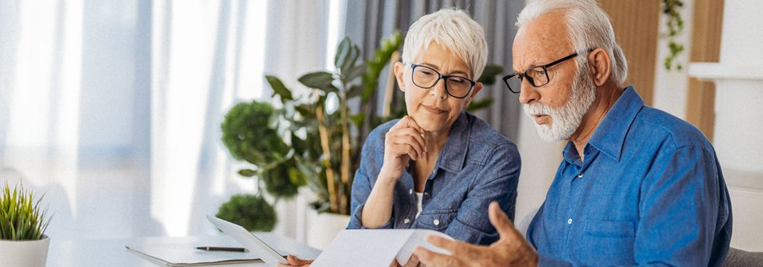 A woman with grey hair and man with grey hair and a beard seated at a table looking at paperwork
