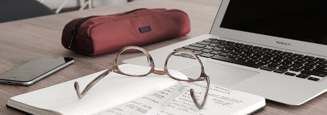 Computer and notebook on a table, with glasses and a pencil case