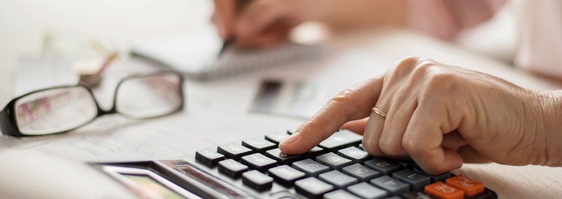 A close up of a woman's hand using a calculator. Her other hand is writing.
