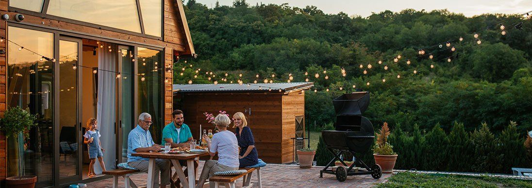 People sitting around a table outdoors with a timber home and bush in the background