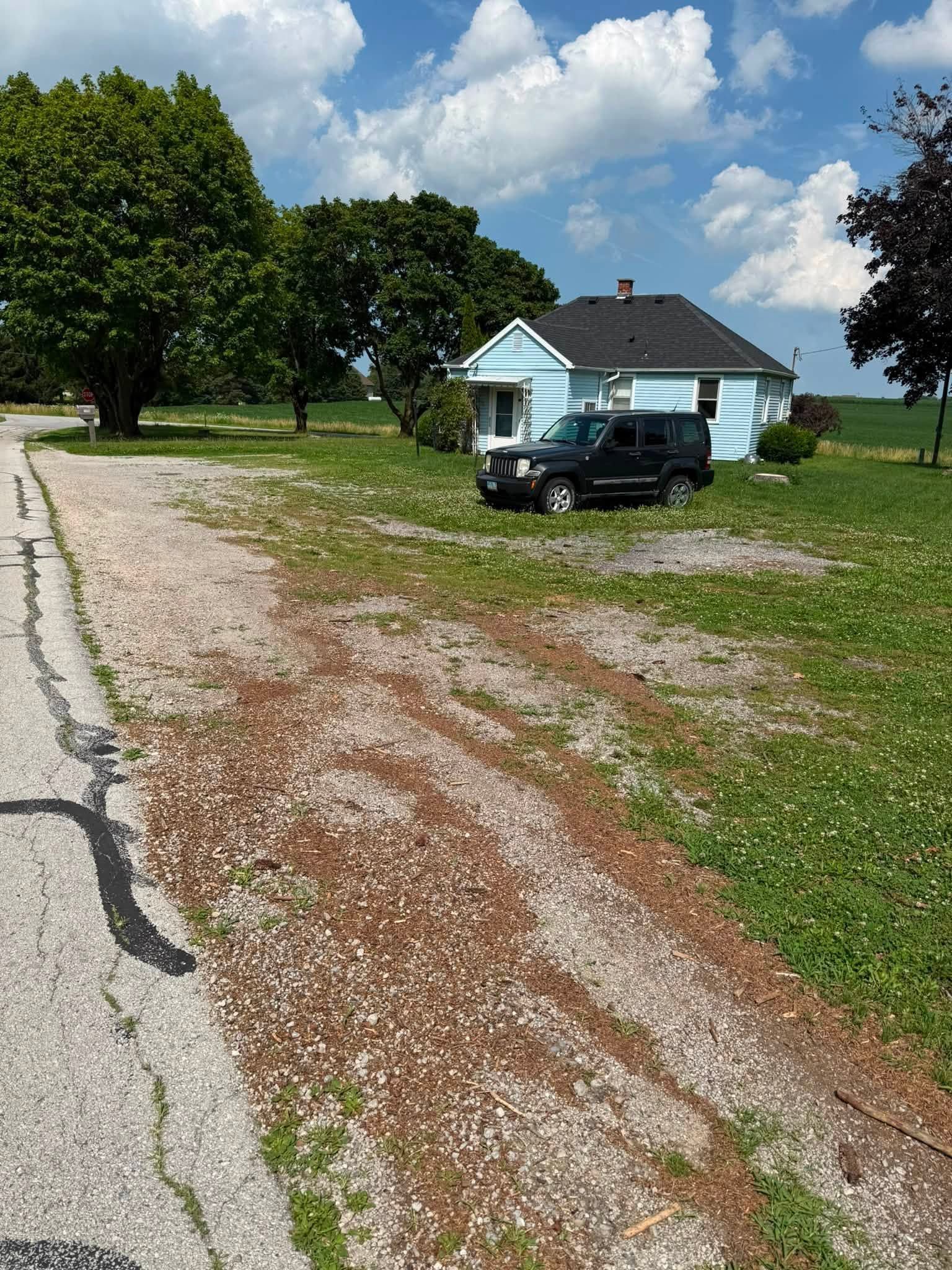 Gravel driveway beside a light blue house with a black SUV, green lawn, and cloudy sky