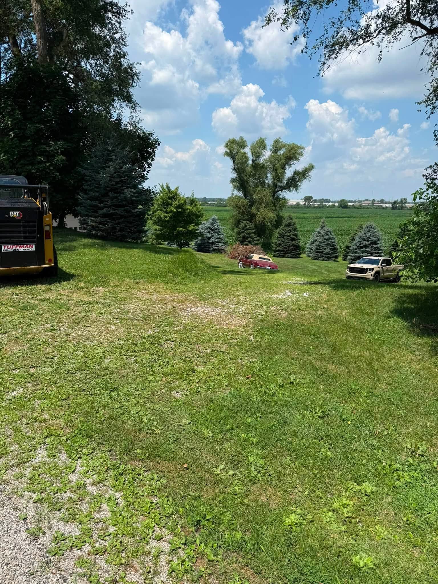 Grassy lakeside yard with trees, blue sky, and two lawn mowers near the water