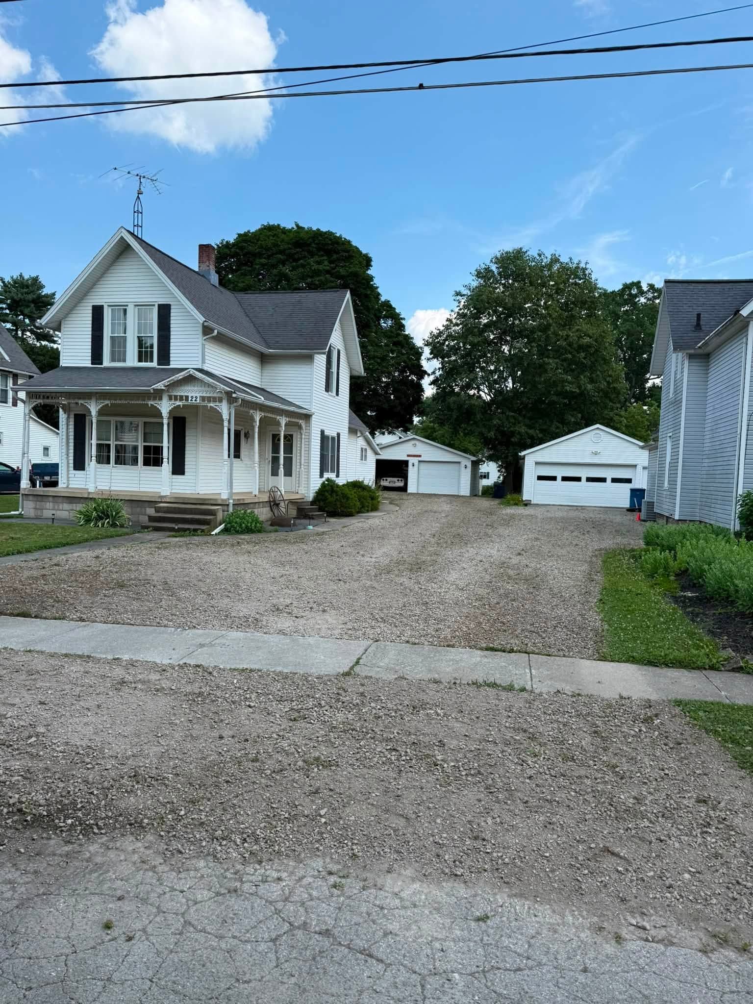 White house with gravel driveway and detached garage under a blue sky.