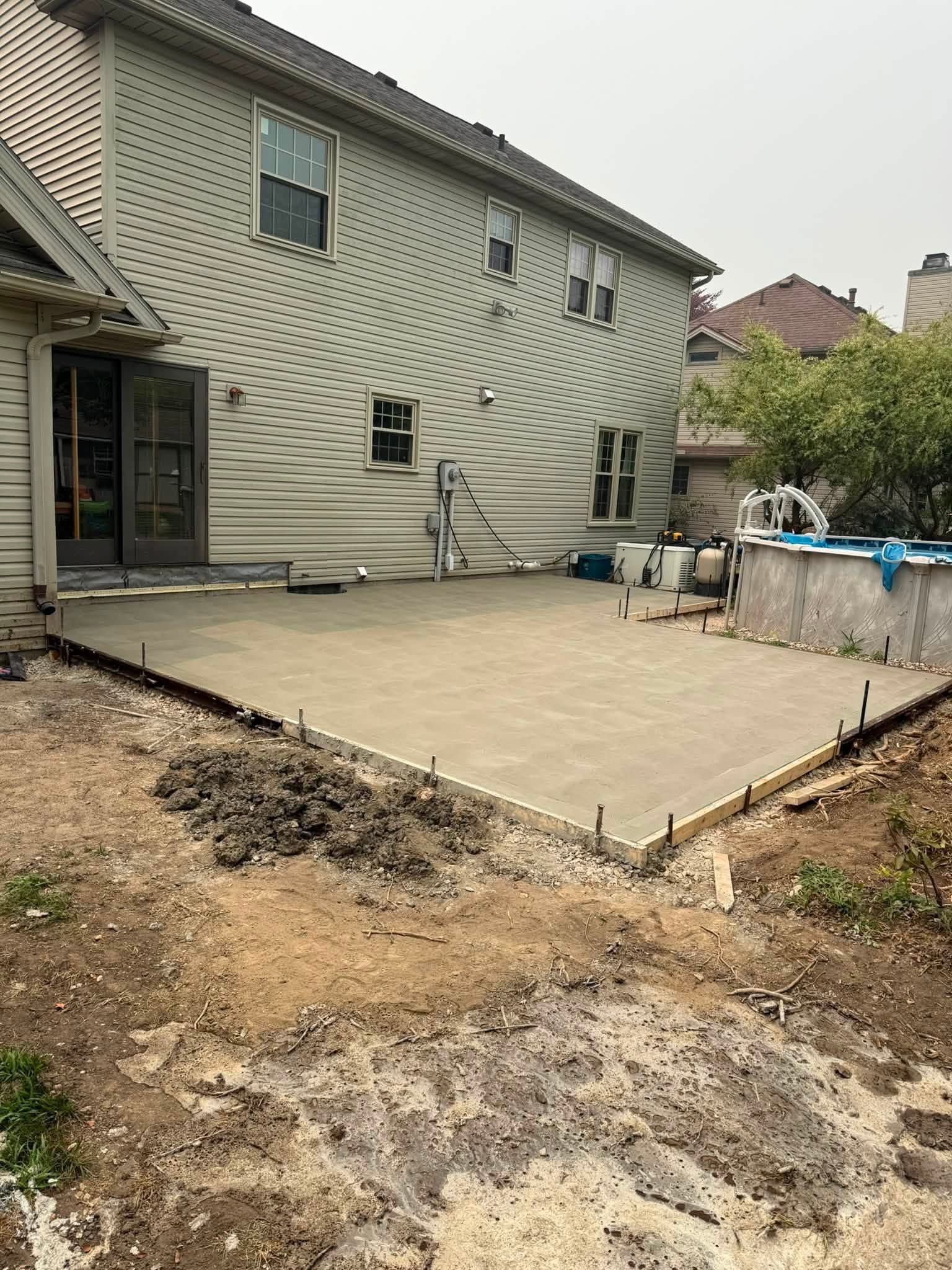 Backyard with a newly poured concrete patio beside a house and a covered pool on the right.