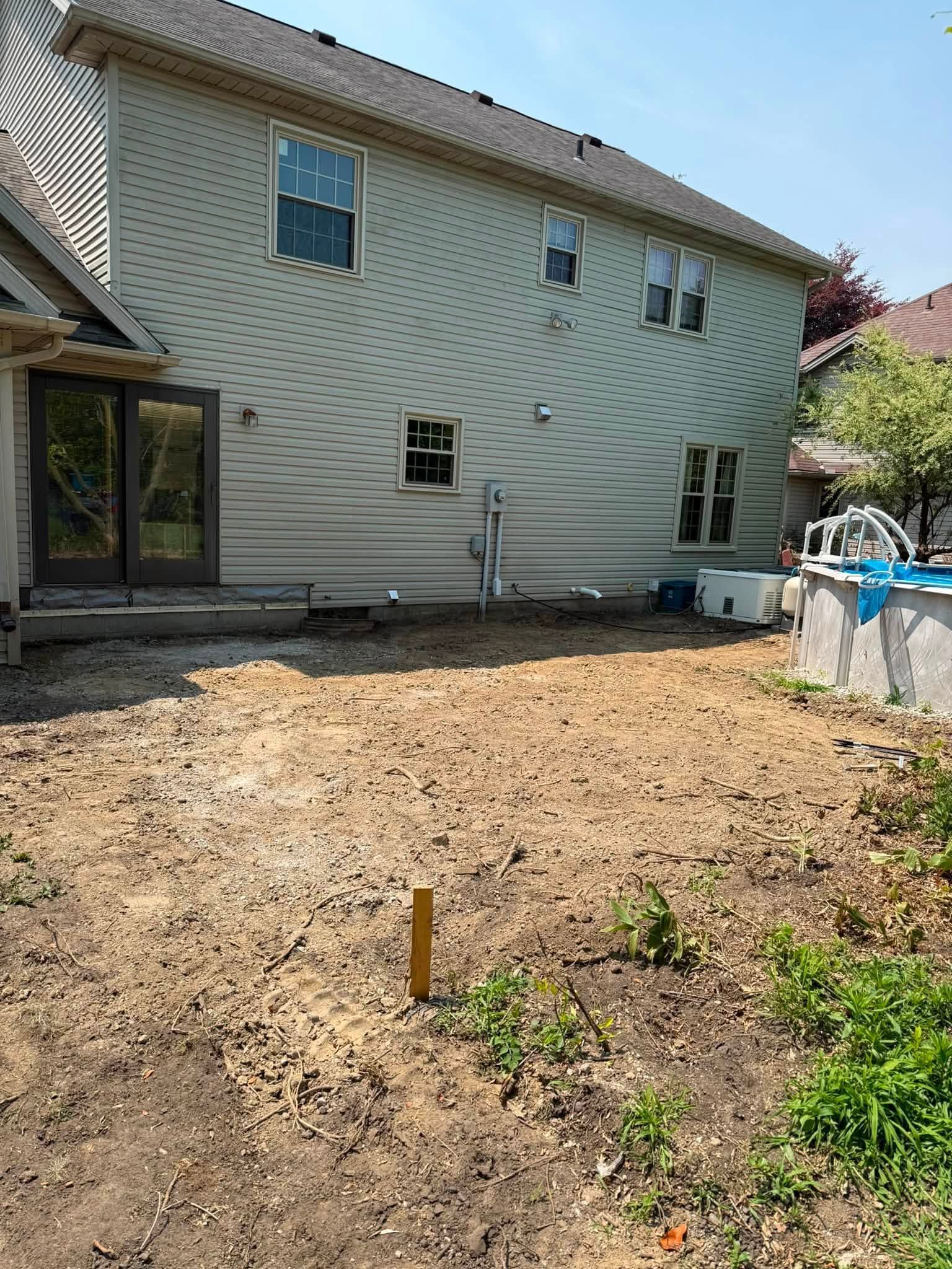 Backyard with bare dirt, a house exterior, and a small patio area with blue-covered items on the right.