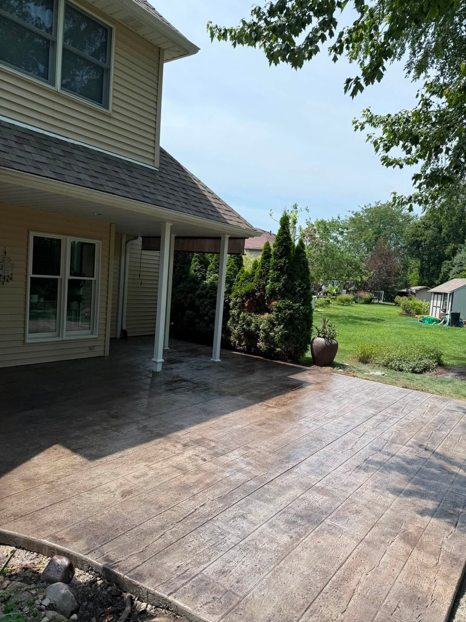 House patio with concrete driveway, beige siding, and a sunny backyard garden.