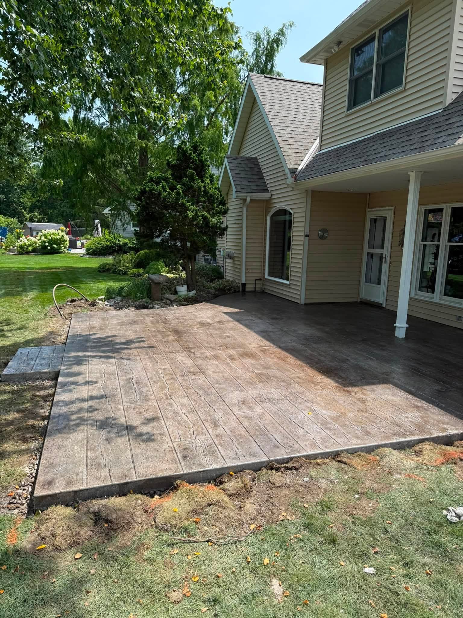 Wooden patio deck beside a beige house with white columns and a shaded tree-lined yard