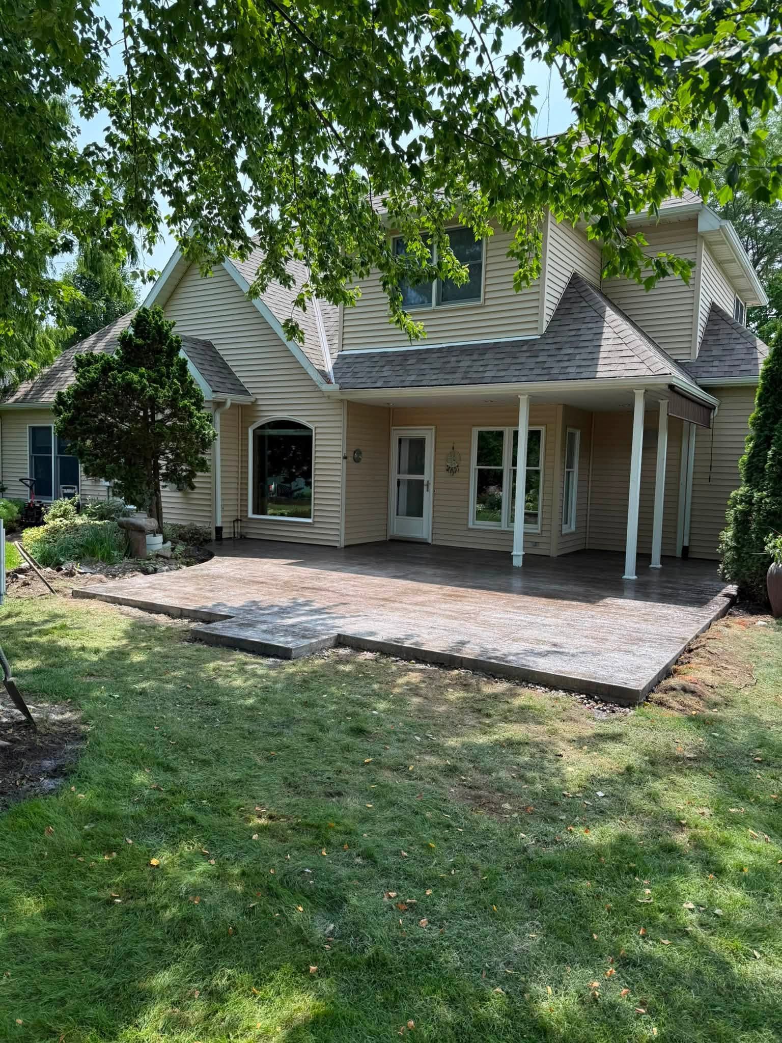 House with shingled roof and covered porch, viewed from a grassy yard under tree shade.