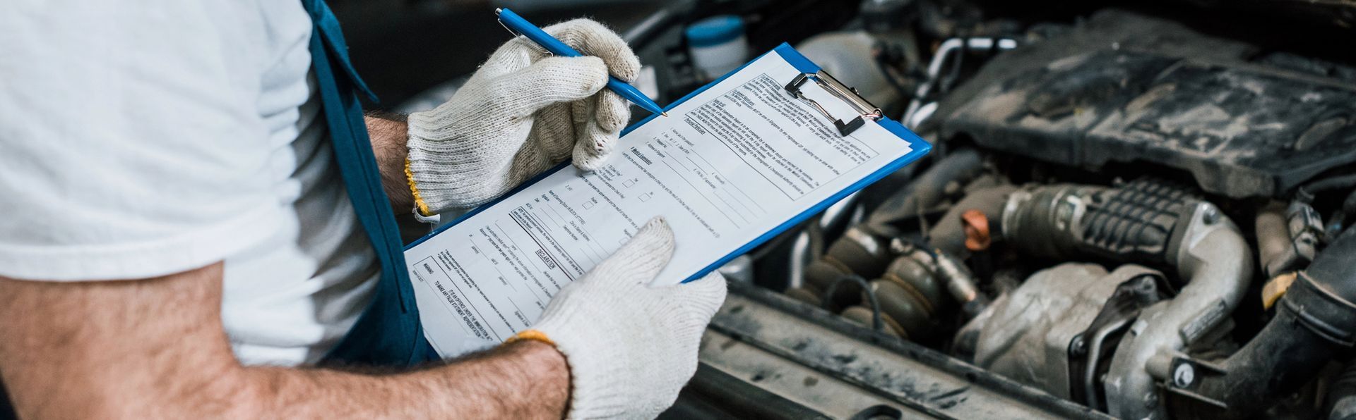 Un meccanico con i guanti bianchi usa una chiave a cricchetto per lavorare sul motore di un veicolo con il cofano aperto in un'officina.