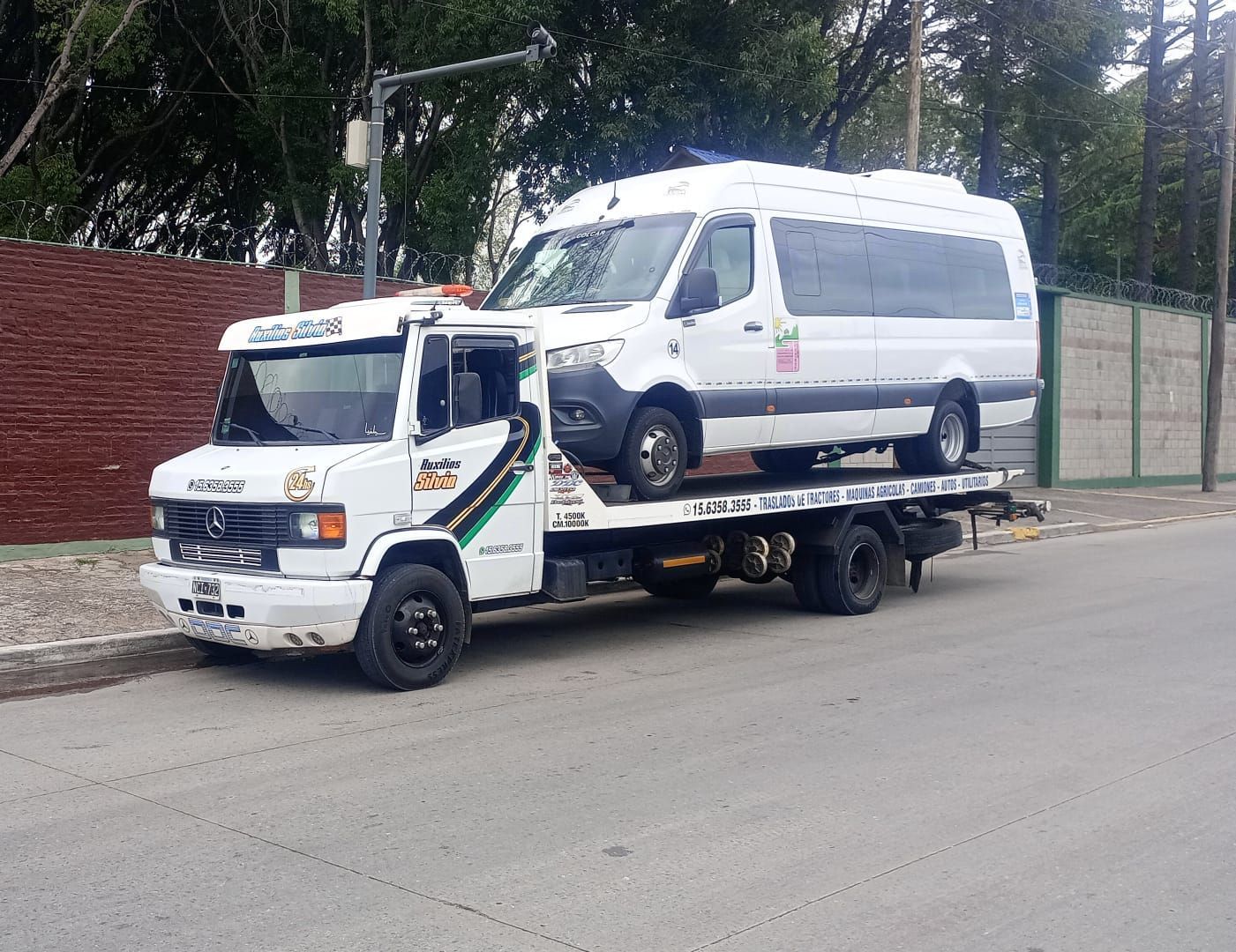 Una grúa amarilla remolca una furgoneta blanca en una calle de la ciudad, junto a edificios de ladrillo.