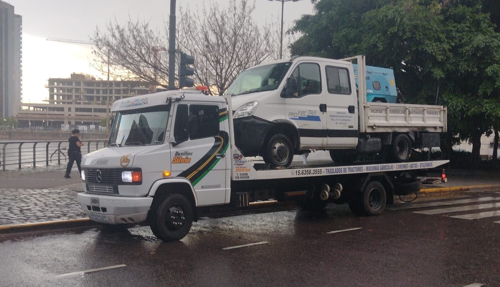 Dos personas hablan con un portapapeles junto a un coche aparcado, mientras un mecánico se interpone entre ellas.