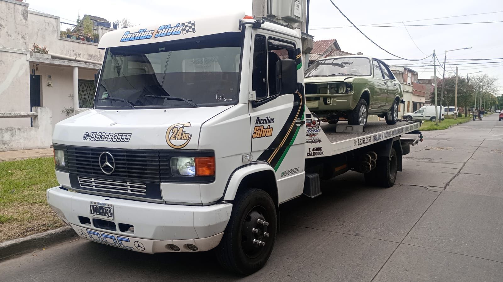 Cuatro camiones de servicios públicos con brazos articulados azules levantados, estacionados en fila al atardecer.