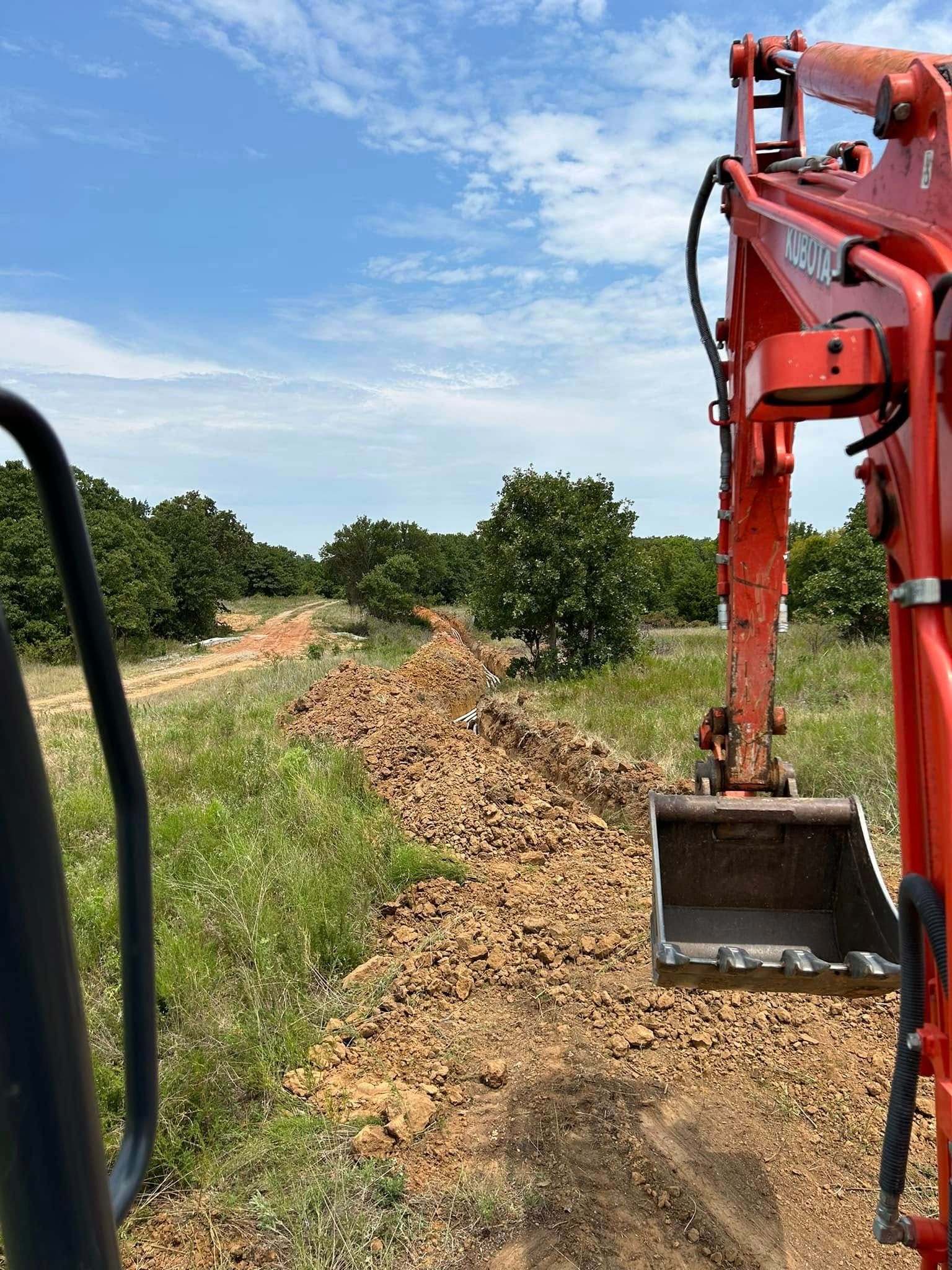 A red excavator is digging a trench in a field.