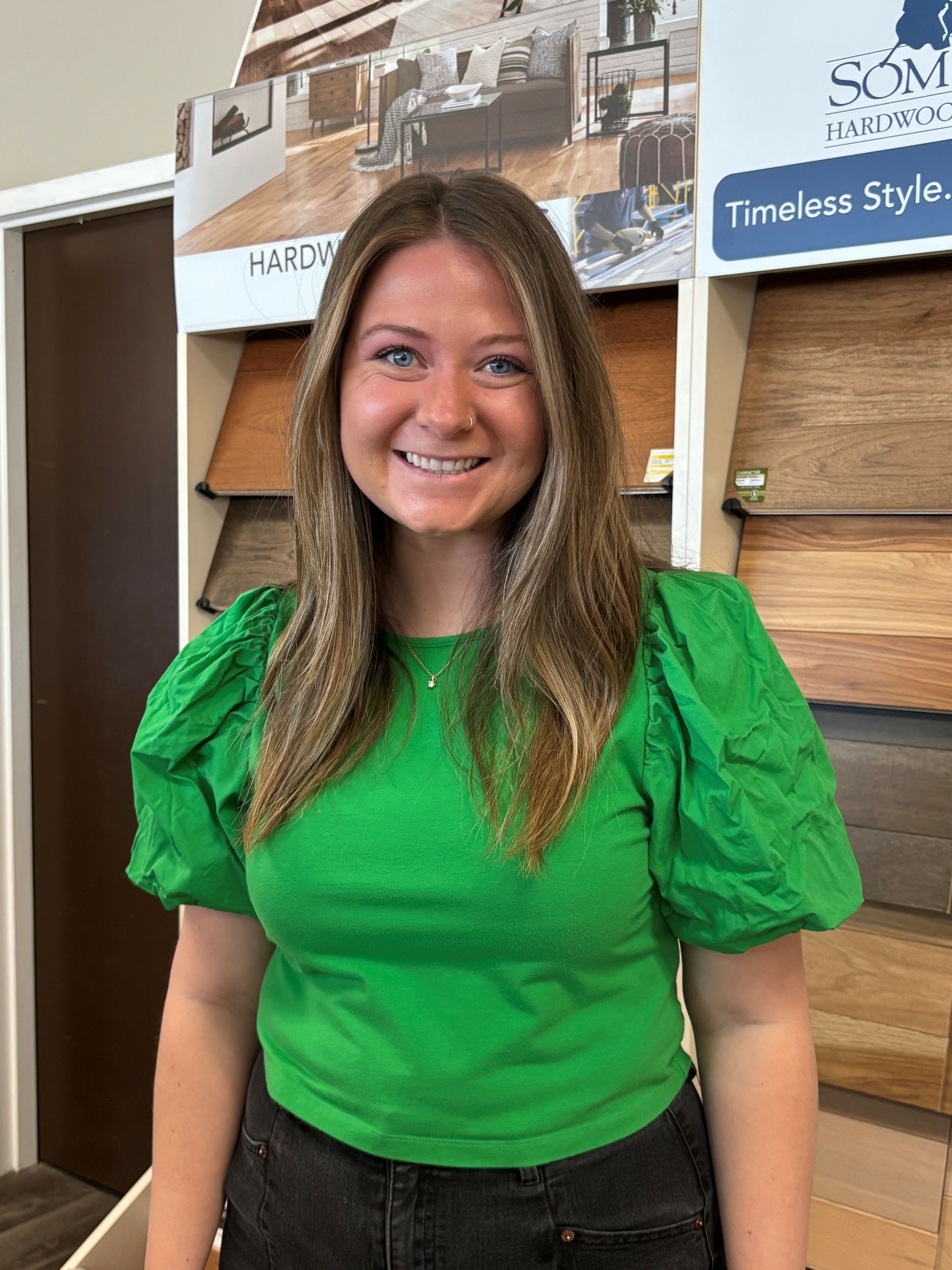 A woman in a green shirt is standing in front of a display of wood flooring.