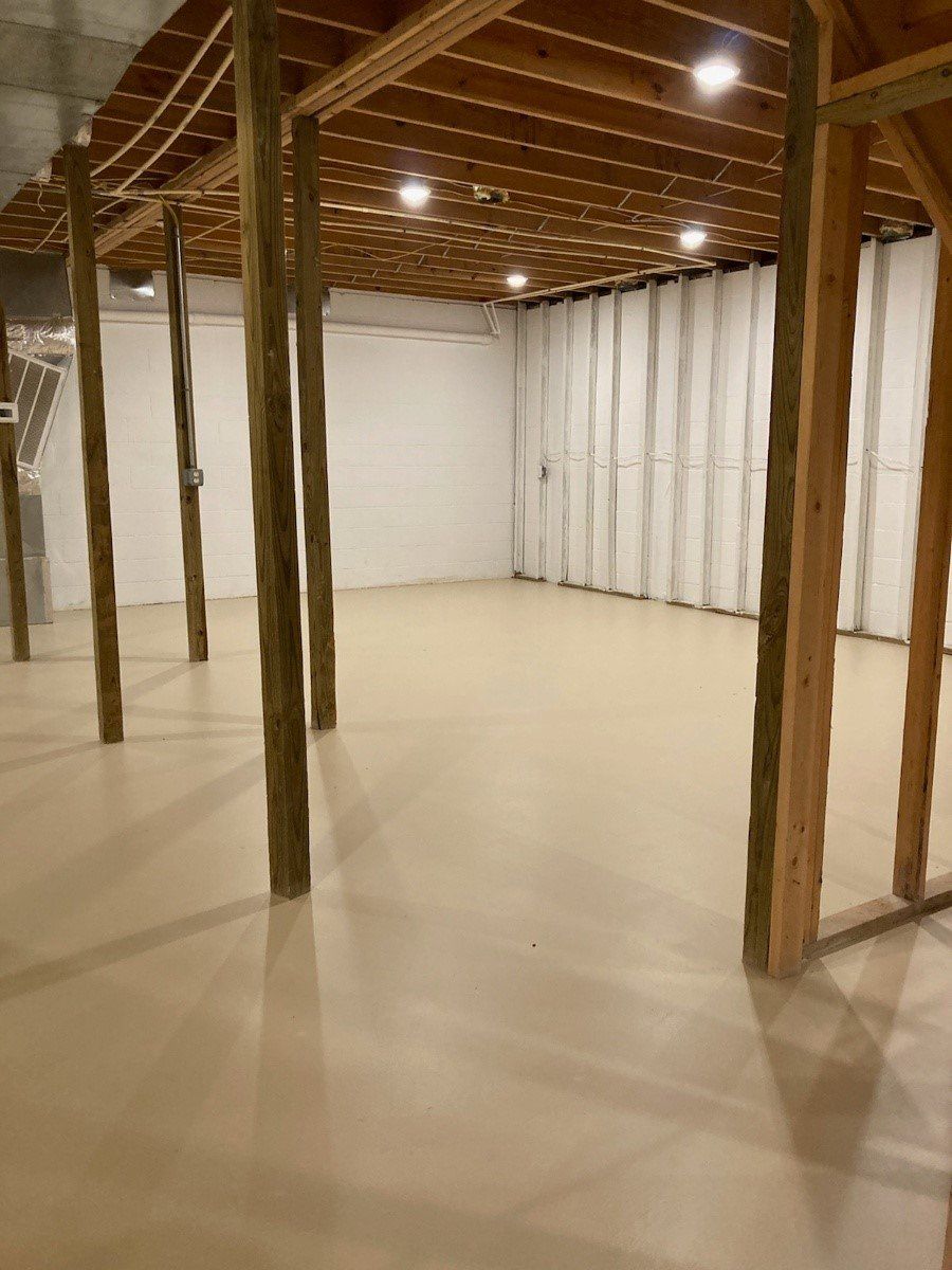 An empty basement with wooden beams and a white floor.