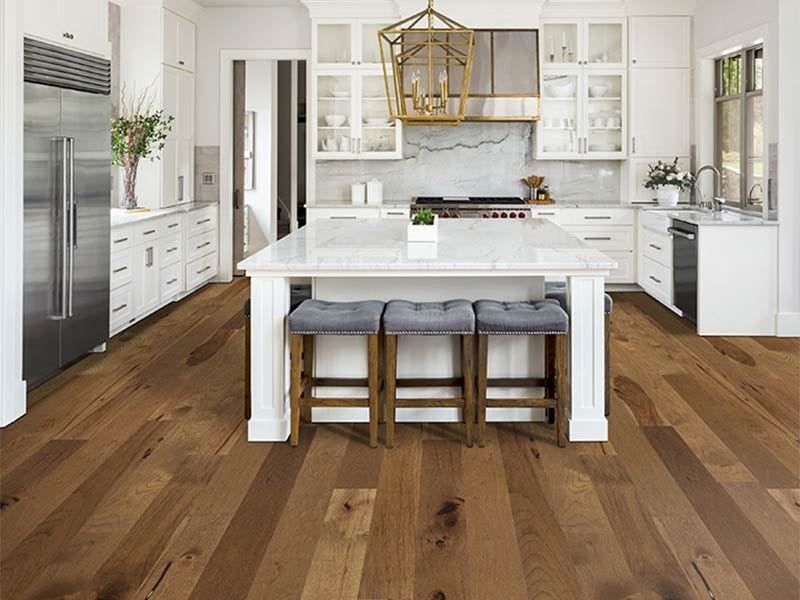 A kitchen with hardwood floors , white cabinets , stainless steel appliances and a large island.