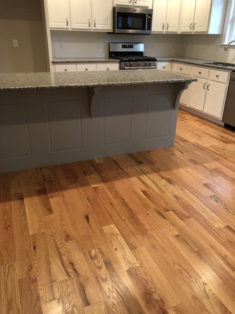 A kitchen with hardwood floors , granite counter tops , stainless steel appliances and white cabinets.