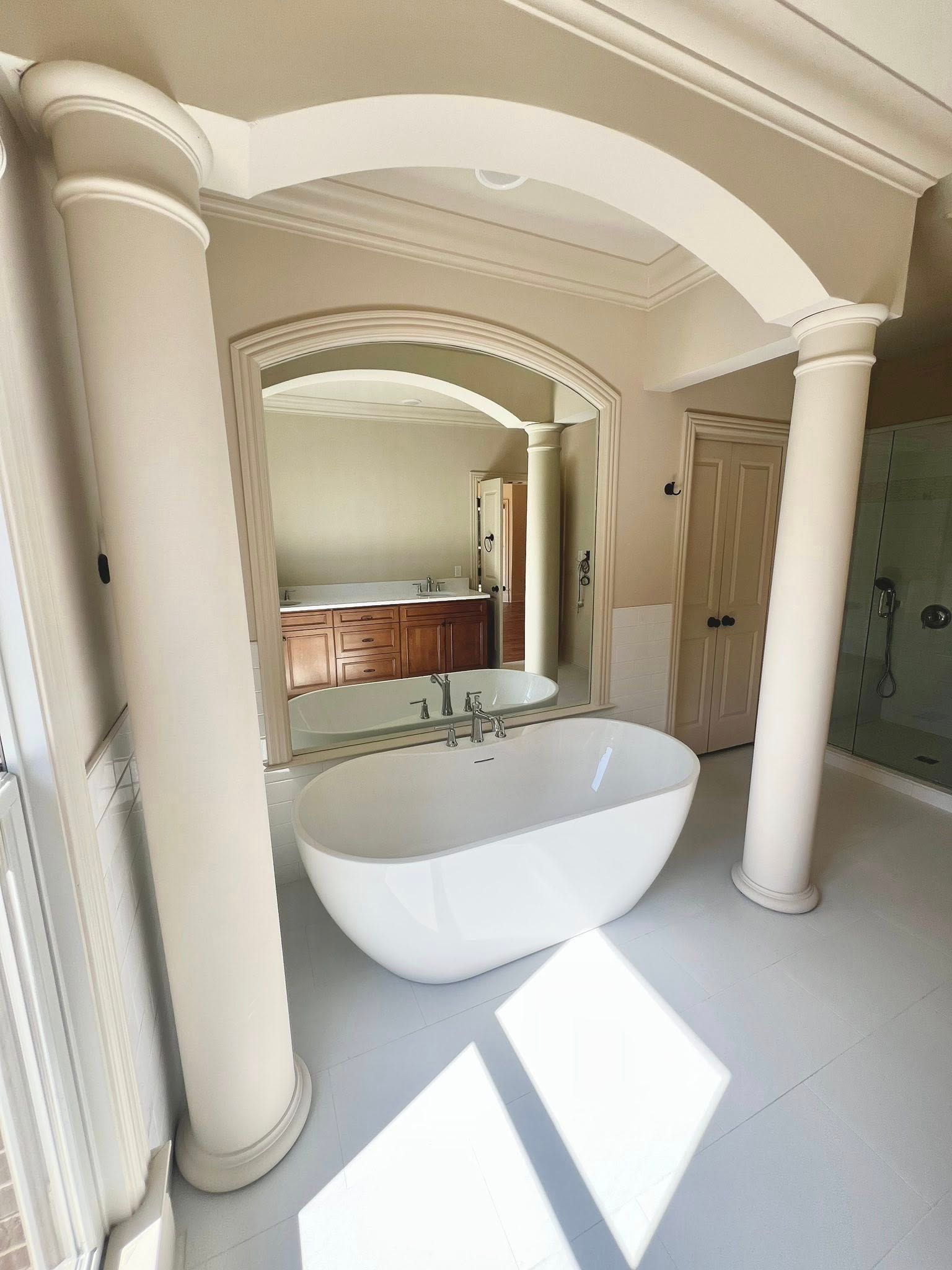 Luxury bathroom with white freestanding tub, columns, arched ceiling, and bright window light