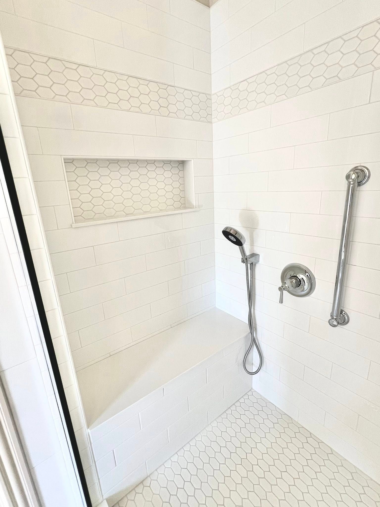 Walk-in shower with white tile, built-in shelf, handheld showerhead, and grab bar
