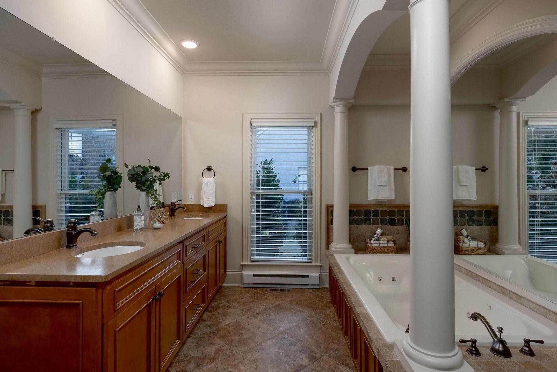 Bright bathroom with wooden vanity, large mirror, and freestanding tub beside a windowed shower area