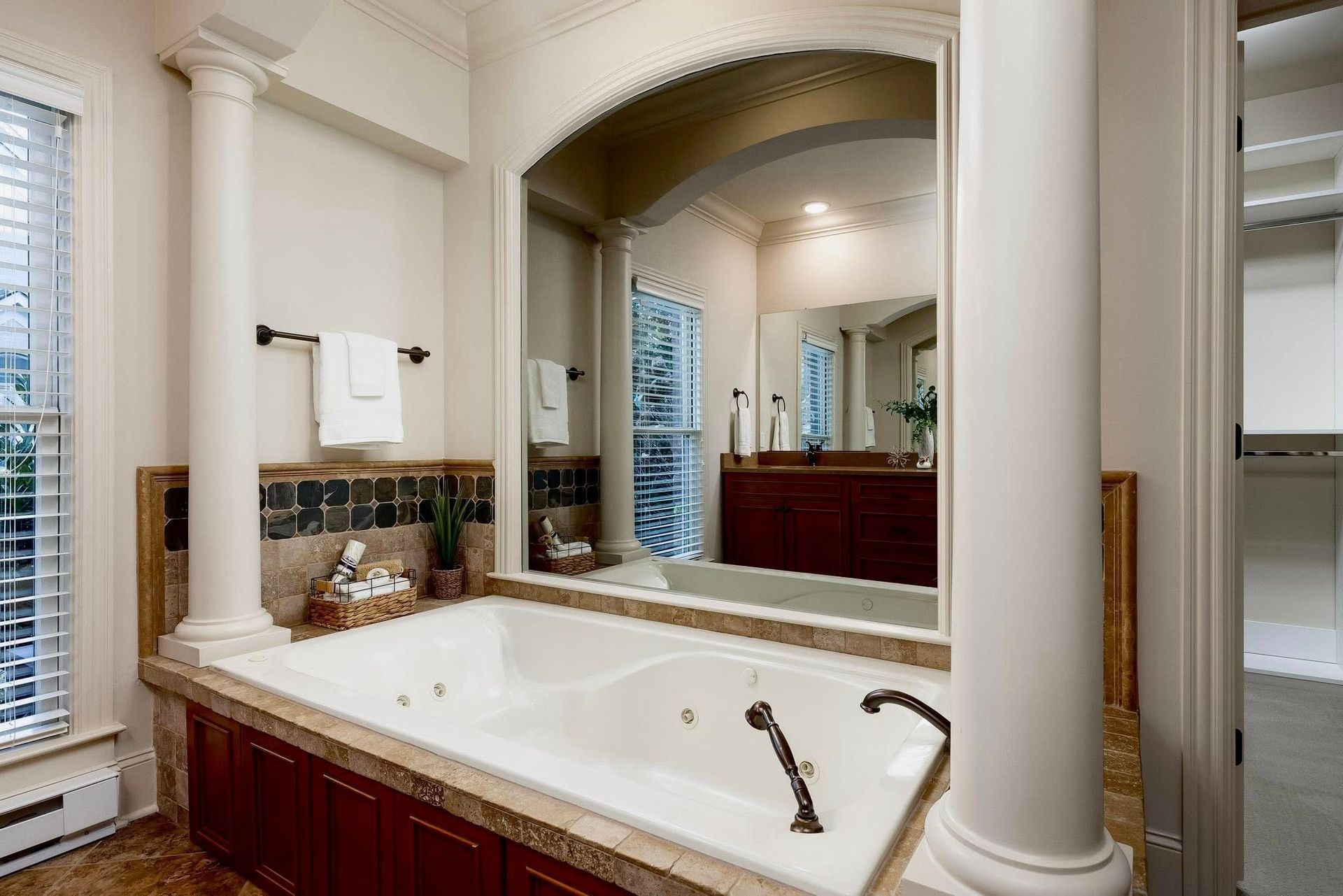 Spacious bathroom with white columns, marble tub, large mirror, and dark wood vanity.